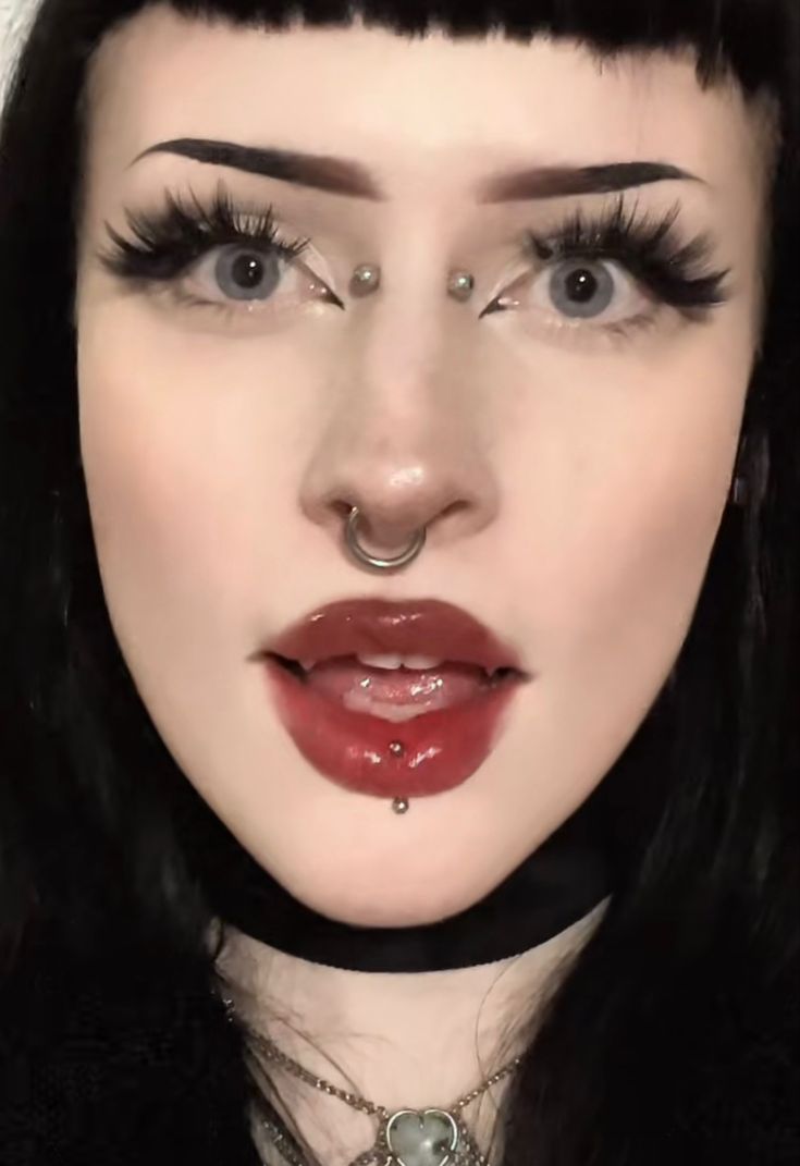 a woman with long black hair and piercings on her nose wearing a choker