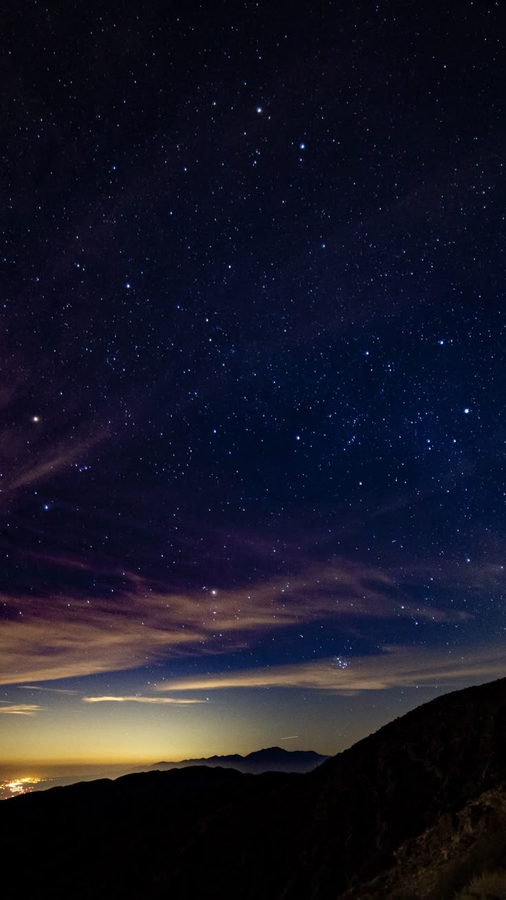 the night sky is filled with stars and clouds, as seen from a hill top