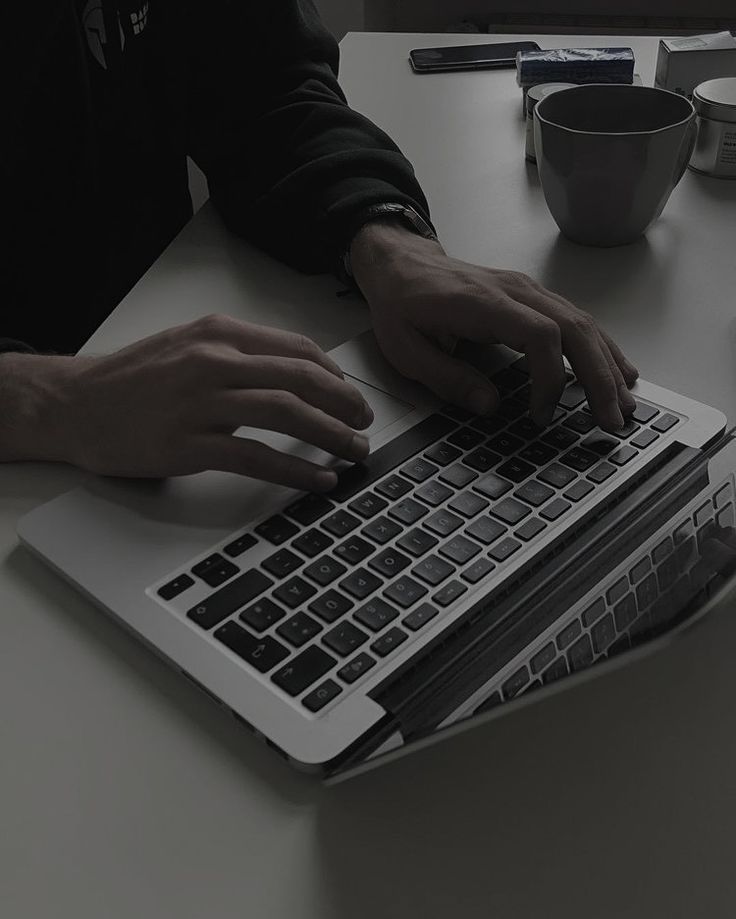 a person typing on a laptop at a table with coffee cups and utensils