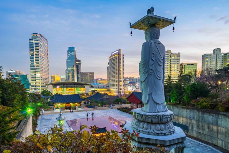 a statue in the middle of a park with buildings in the background