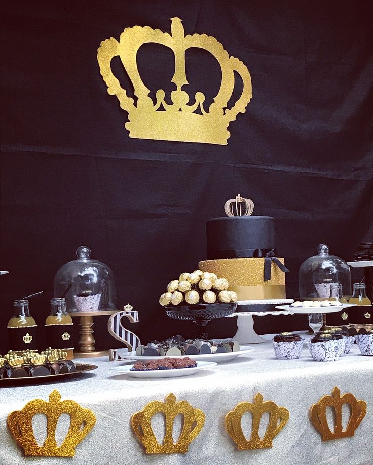 a table topped with cakes and desserts covered in gold foil crown decorations on top of a white table cloth