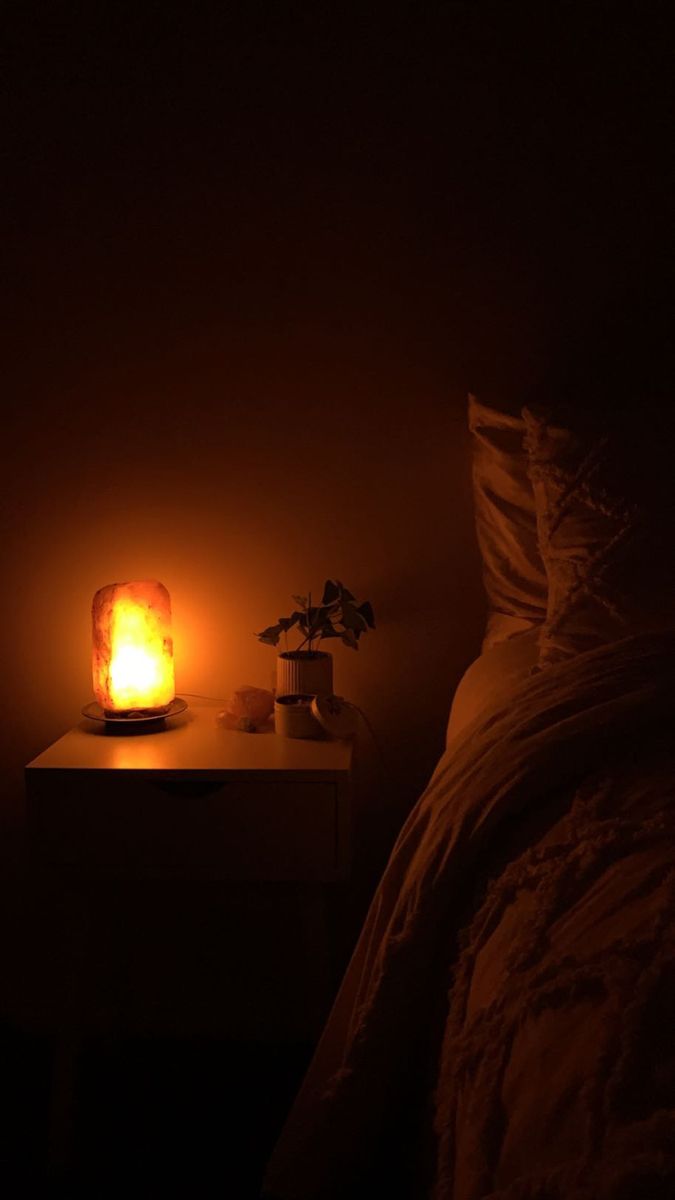 a bed with a night light on top of it next to a small plant in a vase