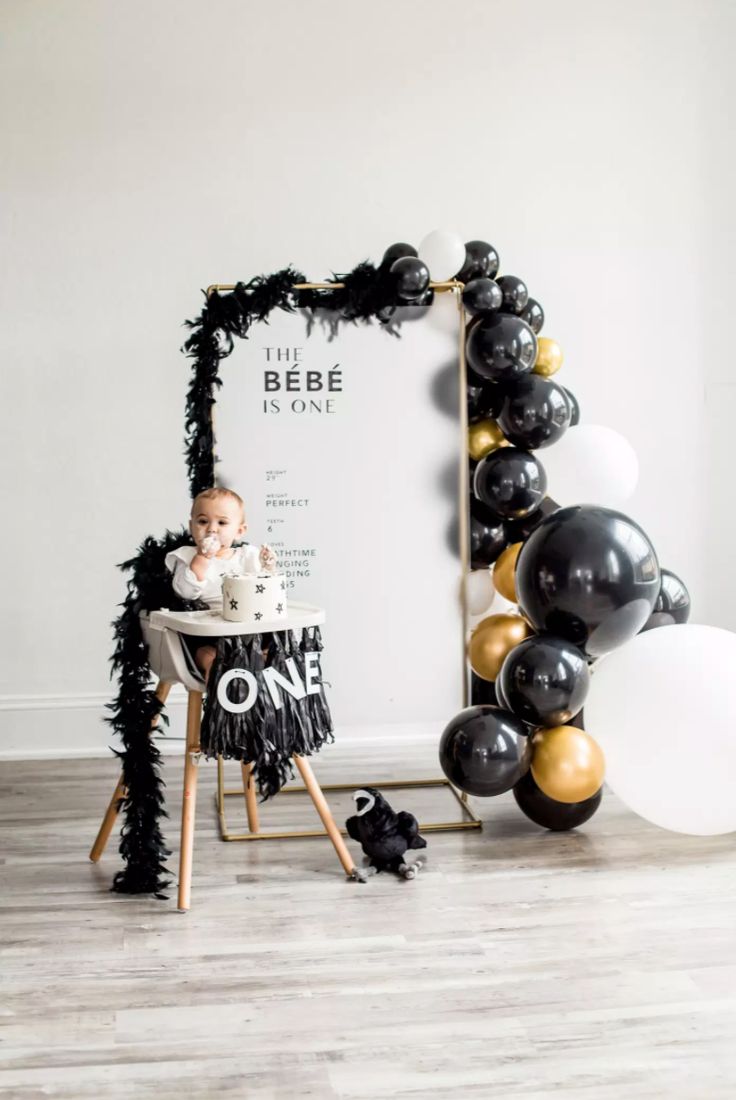 a baby is sitting in a highchair with black and gold balloons around it