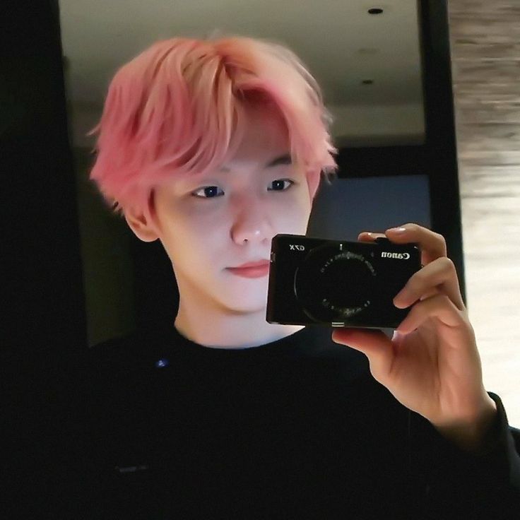 a man with pink hair taking a selfie in front of a mirror holding a camera