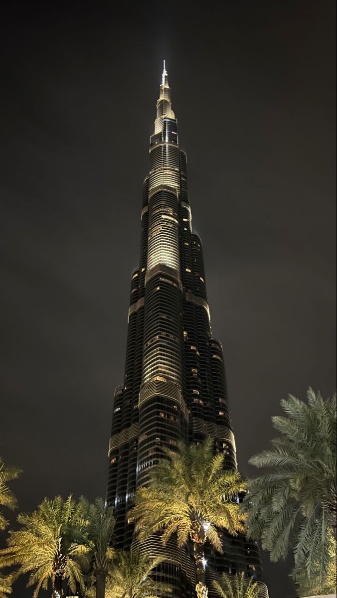 the burj tower is lit up at night with palm trees in front of it