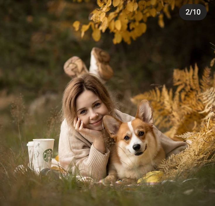 a woman laying on the ground with her dog next to her and holding a coffee cup