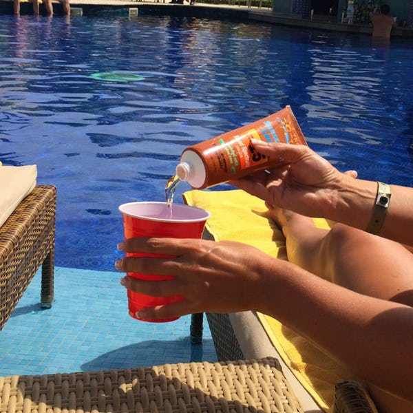 a woman is drinking from a red cup in front of a swimming pool with blue water