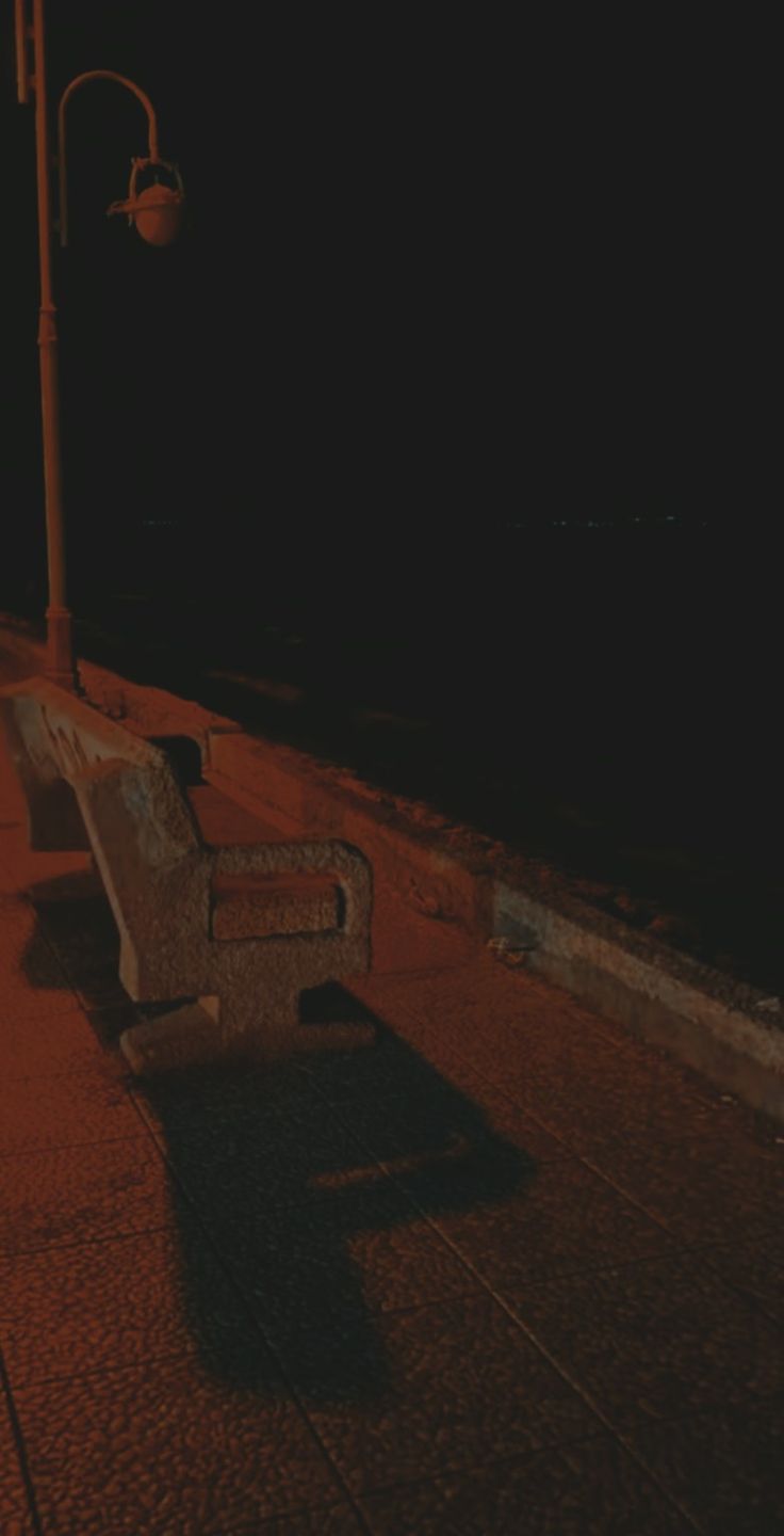 a bench sitting on the side of a road next to a street light at night