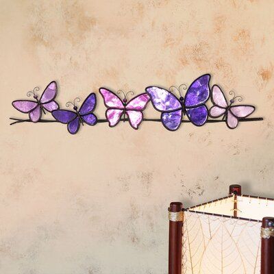 a metal wall hanging with purple butterflies on it's side next to a lamp