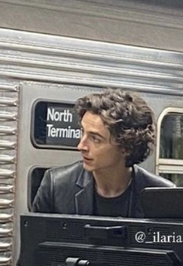 a man sitting on a train looking out the window at another person standing next to him