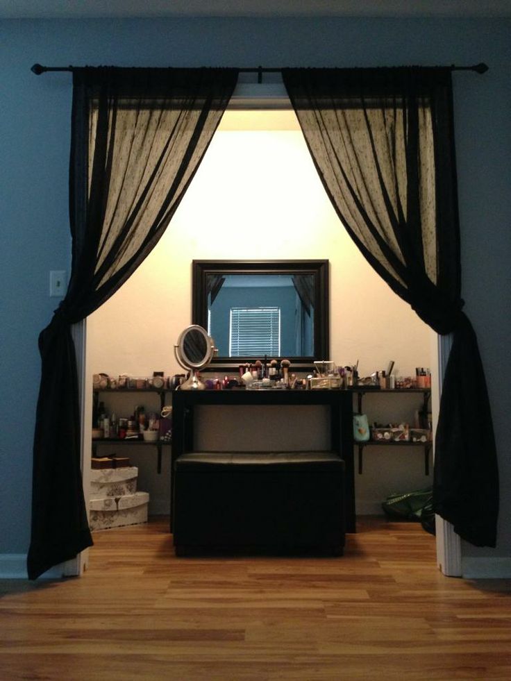 a room with a desk, mirror and black curtained window in the middle of it