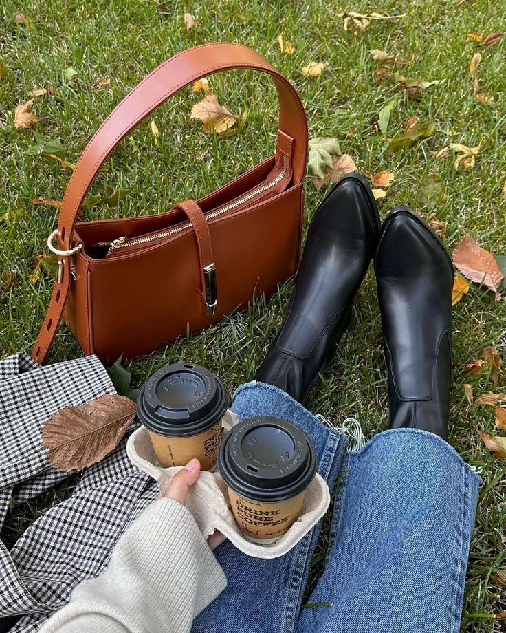 a woman is sitting on the grass with her purse and coffee in front of her