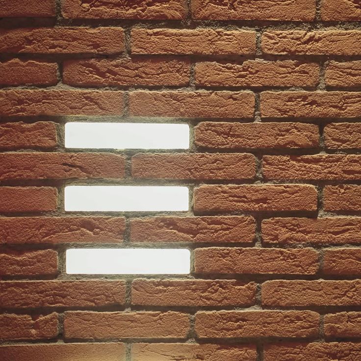 a brick wall with three windows in the middle and one light shining on it's side