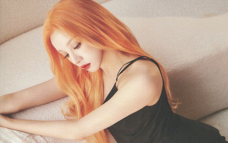 a woman with long red hair sitting on a couch looking at her cell phone while wearing a black tank top