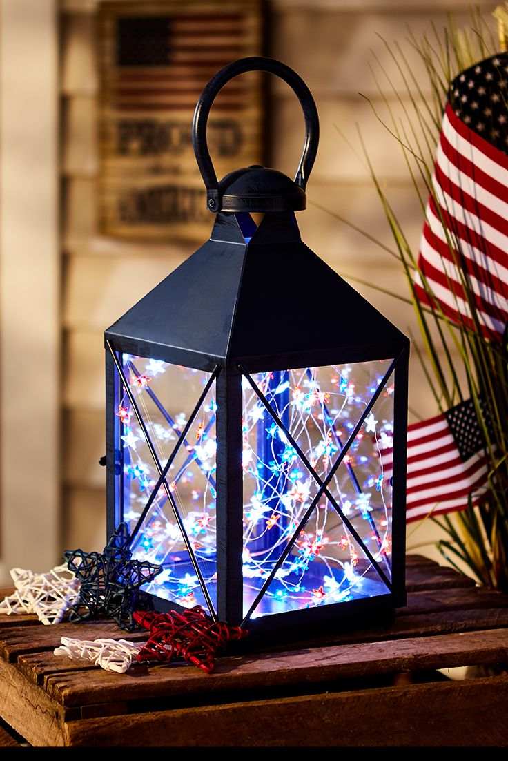 a lit up lantern sitting on top of a wooden table next to an american flag