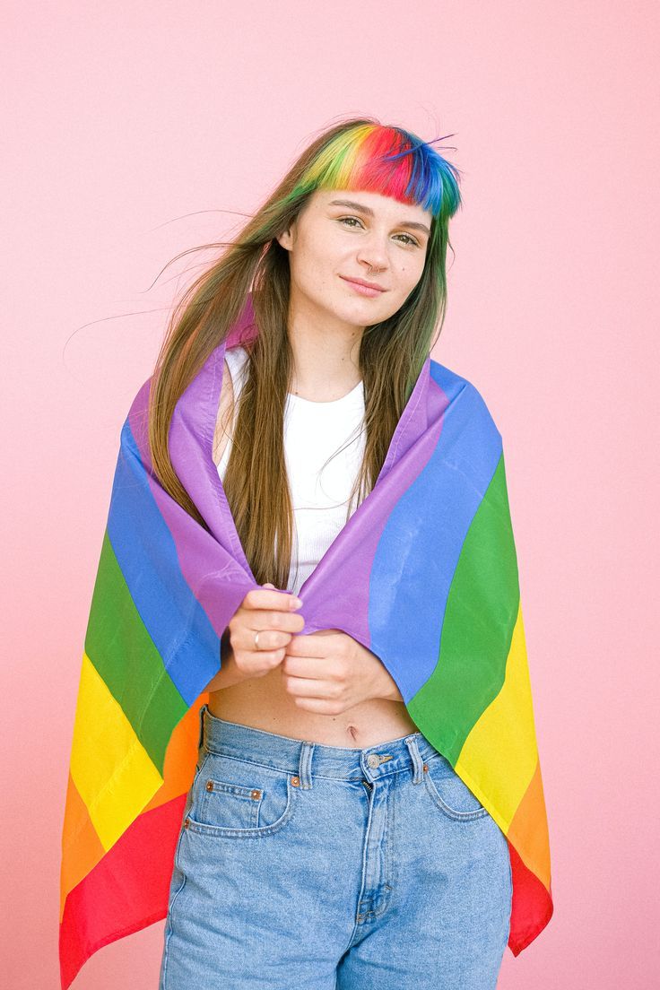 a young woman with colorful hair wearing a rainbow colored shawl over her shoulders and looking at the camera