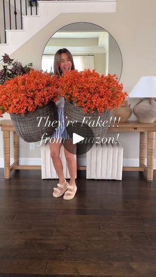 a woman standing in front of a mirror holding two large baskets filled with orange flowers