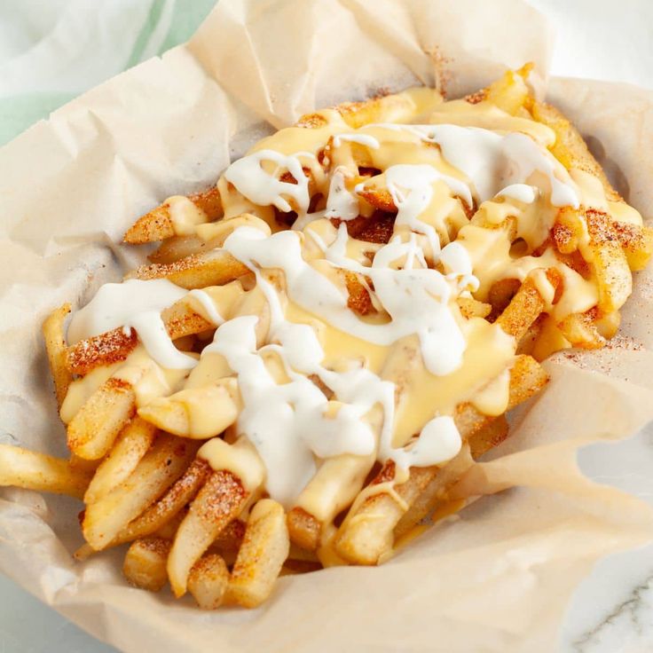 a basket filled with french fries covered in cheese and sour cream on top of paper