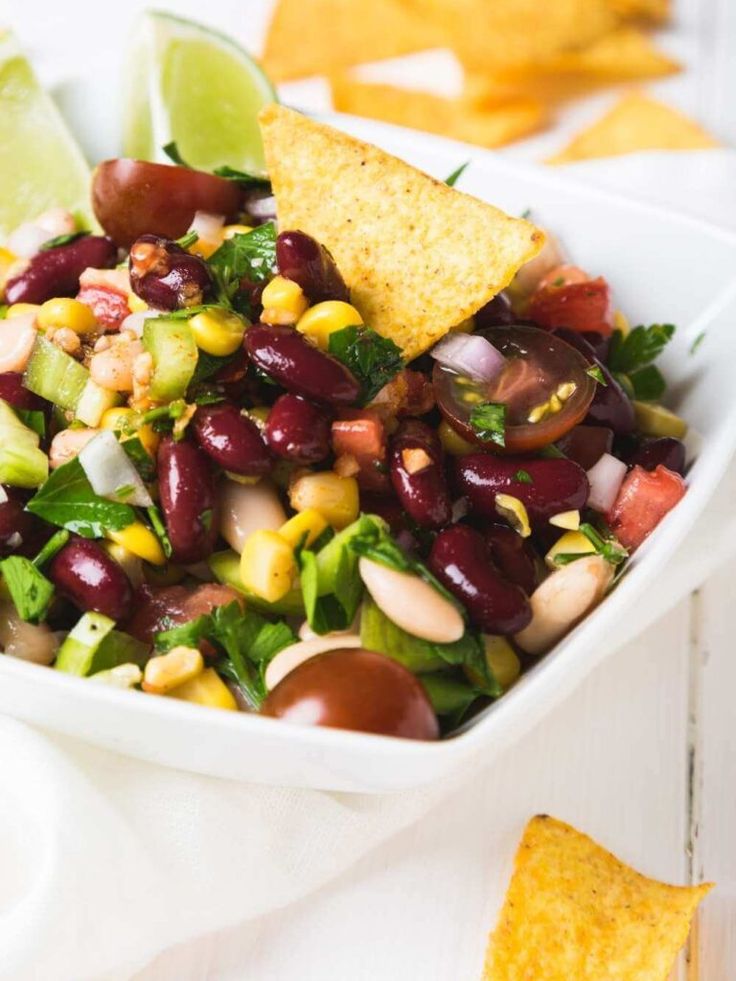 a white bowl filled with beans and corn next to tortilla chips on top of a table