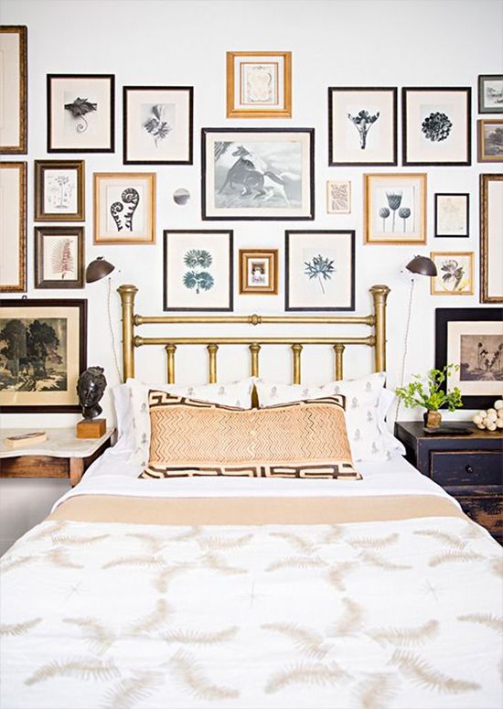 a bedroom with many framed pictures on the wall above the bed and below the headboard