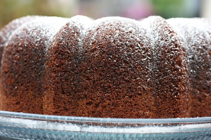 a bundt cake with powdered sugar on top sits in a glass dish, ready to be eaten