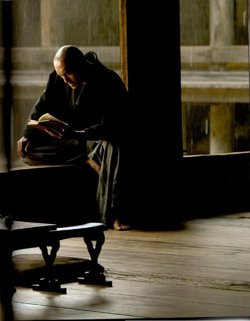 an old man sitting on a bench reading a book in the middle of a room