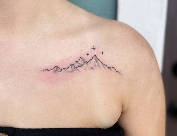 a woman's shoulder with a mountain tattoo on the left side of her chest