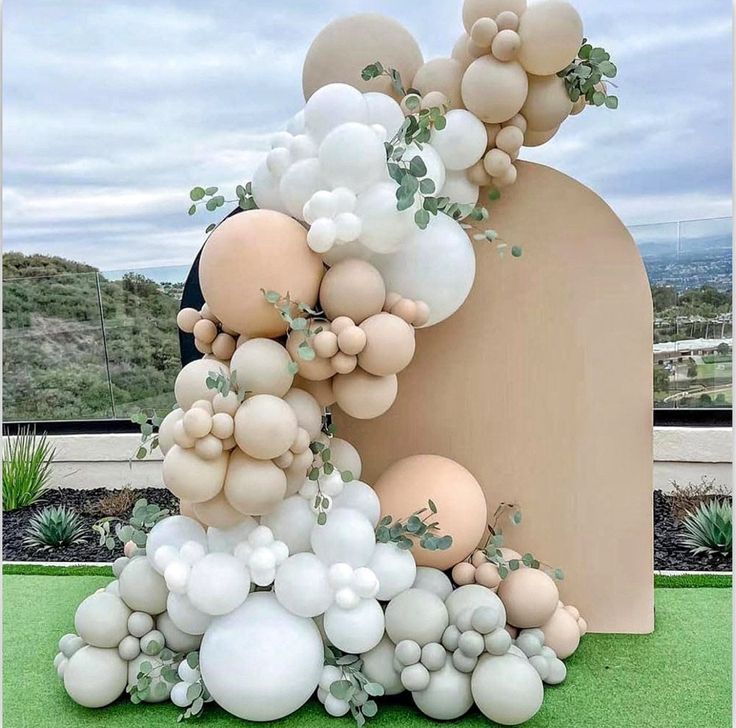 an arrangement of balloons and greenery in front of a large sculpture on the grass