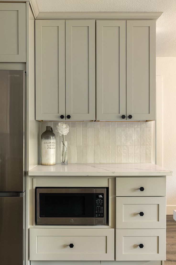 a kitchen with gray cabinets and white counter tops, silver refrigerator and microwave in the corner