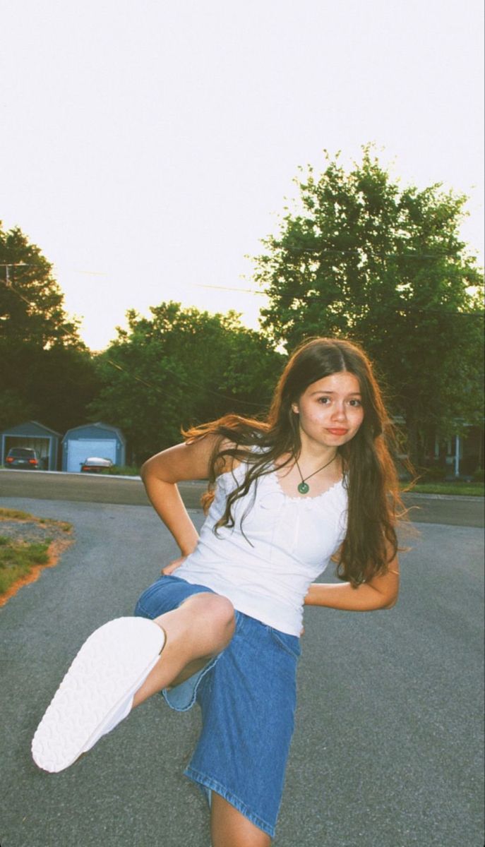 a young woman is posing on the street with her skateboard