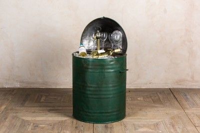 a green trash can filled with bottles and empty wine glasses on top of wooden floor