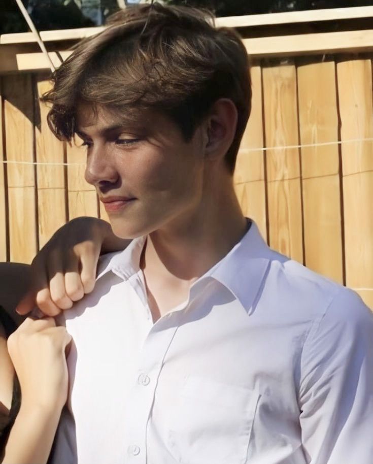 a young man and woman standing next to each other in front of a wooden fence