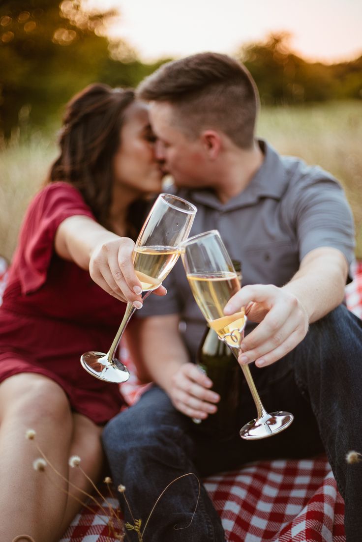 a man and woman sitting on a blanket holding wine glasses with champagne in each hand