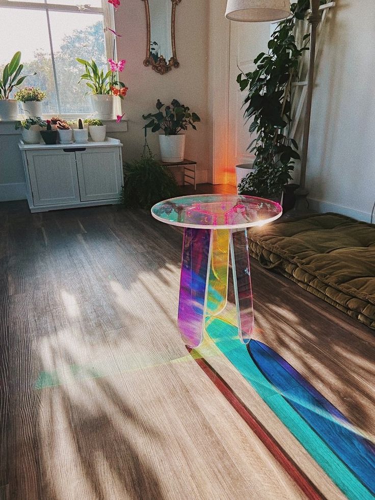 a glass table sitting on top of a hard wood floor next to a plant filled window