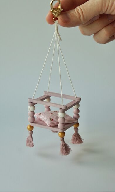 a hand holding a miniature dollhouse swing with beads and tassels on it