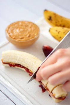 a person cutting up a banana on top of a white plate with peanut butter and jelly