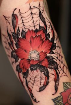 a woman's leg with a spider web and red flower tattoo on the thigh