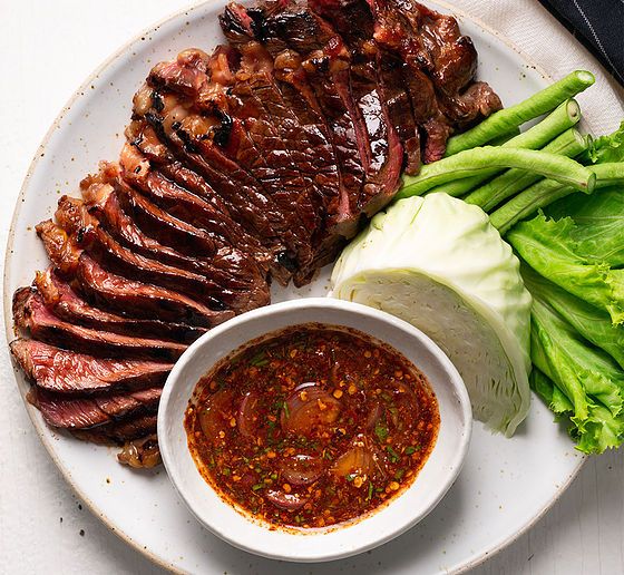 a white plate topped with meat and veggies next to a bowl of sauce