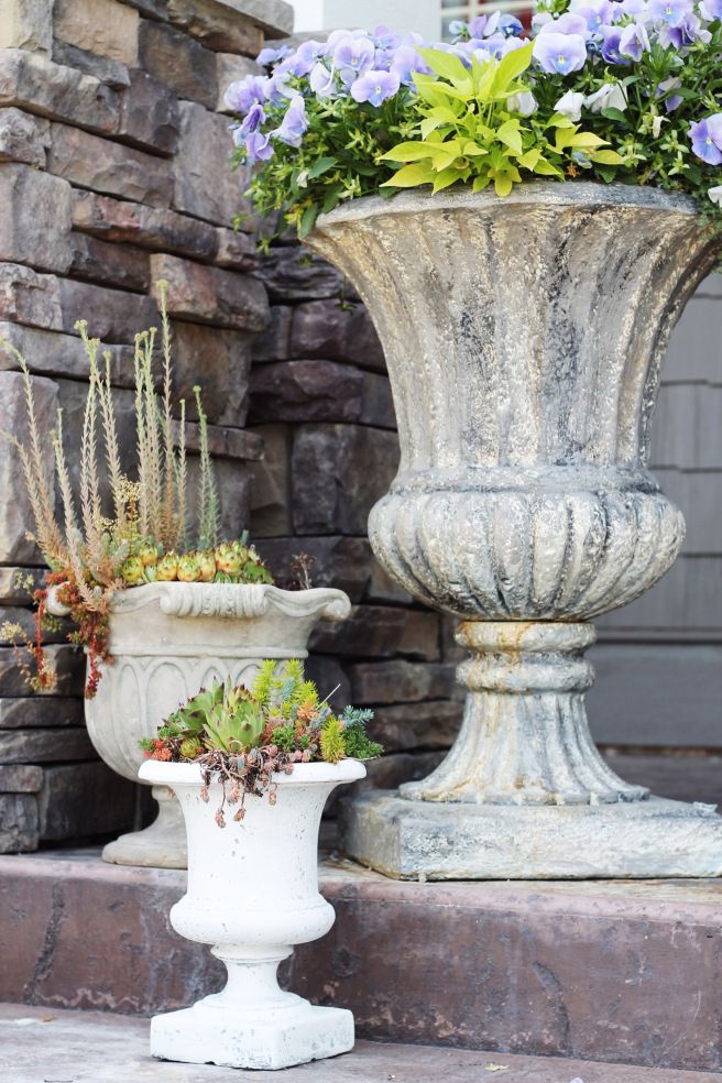 two large white vases with flowers in them sitting on the side of a building