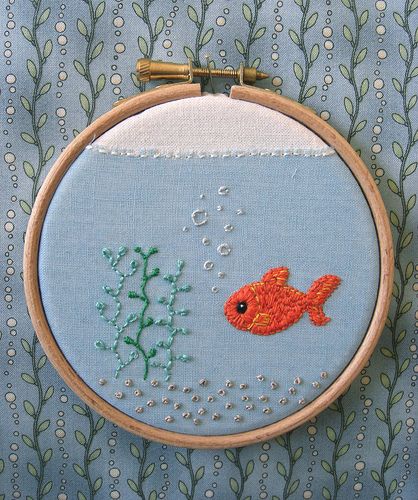 an embroidered fish and seaweed on a blue background with gold thread in the hoop