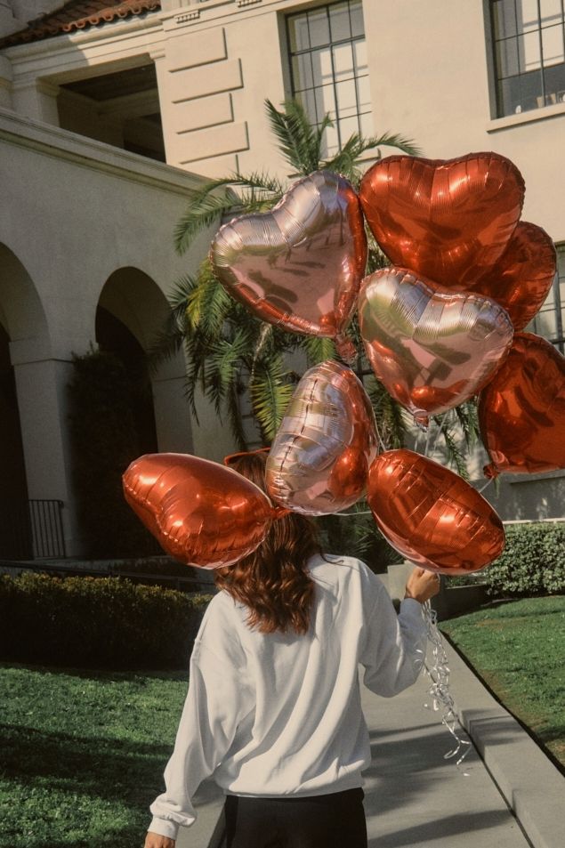 a woman is walking down the sidewalk with many balloons on her head and she has long hair