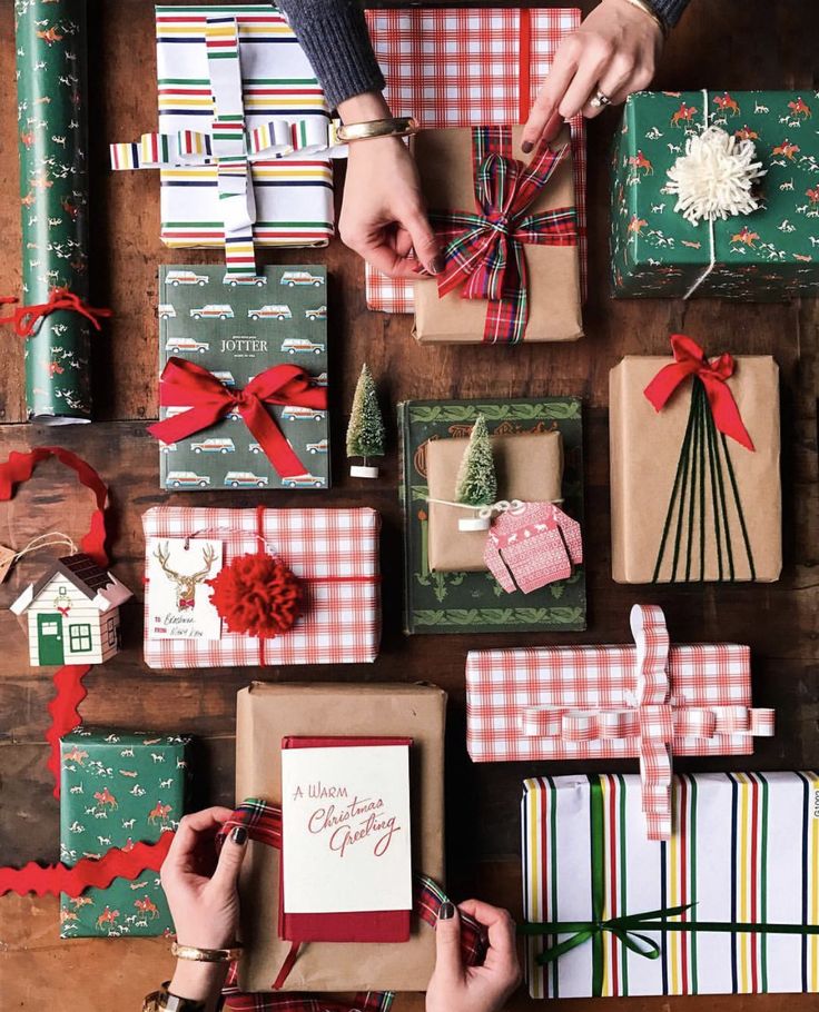 someone wrapping christmas presents on a table with red and green ribbon around the gift boxes