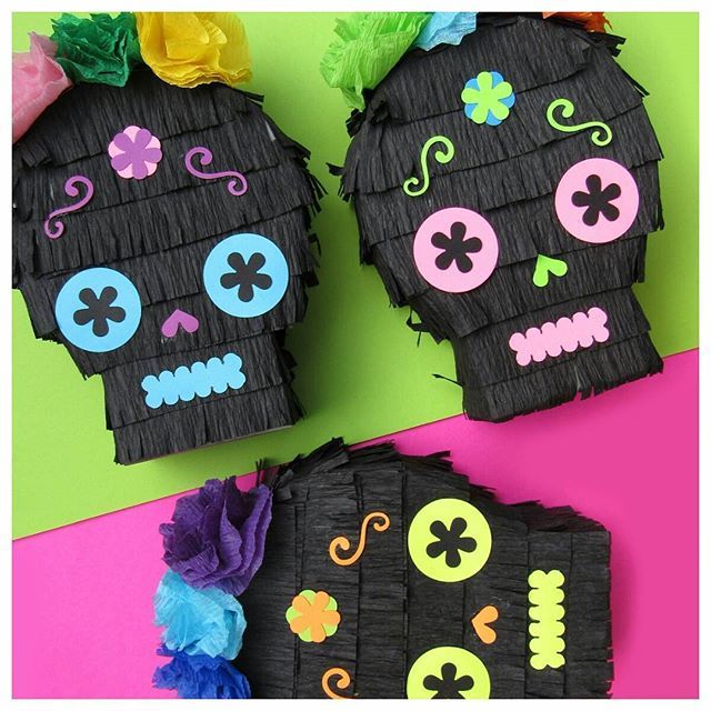 two paper skulls with flowers on them sitting next to each other in front of a green and pink background