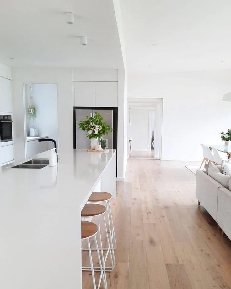 a white kitchen and living room with wood flooring, counter tops and bar stools