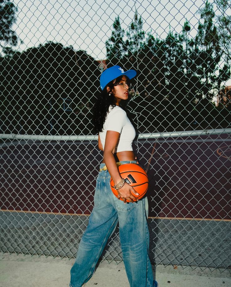 a woman holding a basketball in her right hand while standing next to a chain link fence