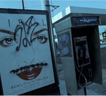 two telephones with graffiti on them are next to each other in front of a gas station