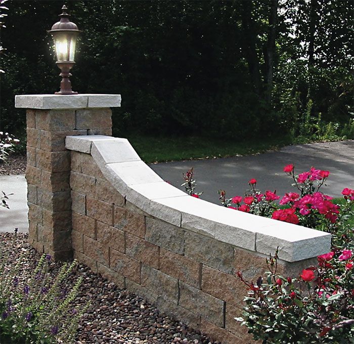 a stone bench sitting next to flowers and a street light on top of a brick wall