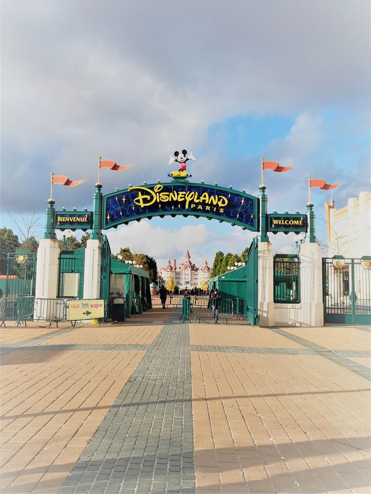 the entrance to disneyland world with flags flying in the air and people walking under it