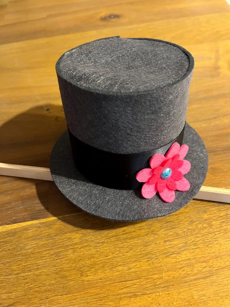 a gray hat with a pink flower on it sitting on a wooden table next to a pencil