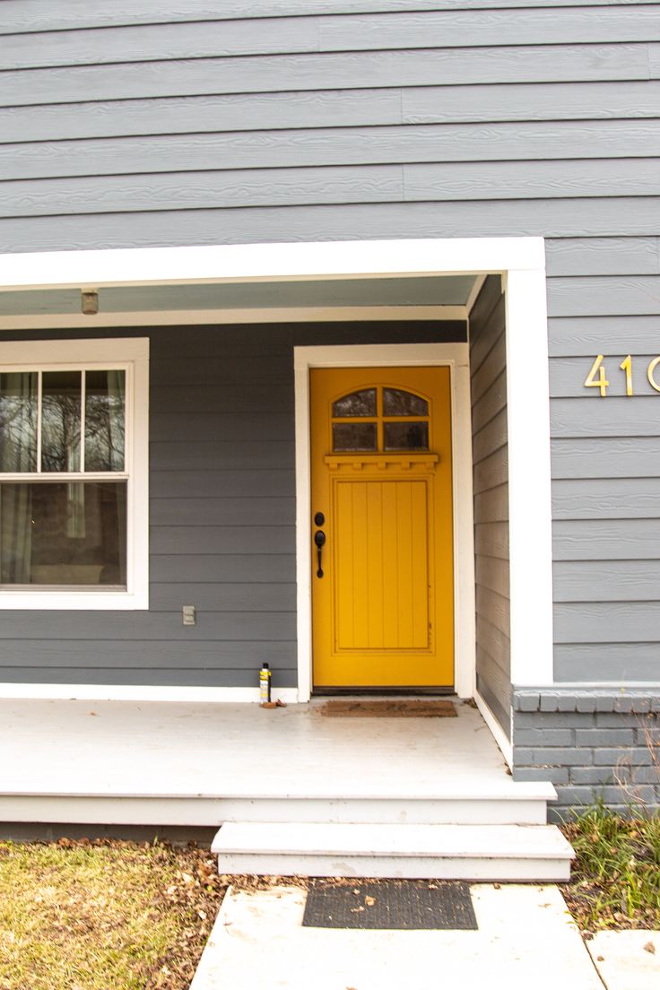 a yellow door sits on the front porch of a gray house with steps leading up to it